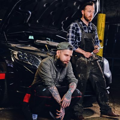 two-bearded-tattooed-mechanics-near-the-car-in-a-workshop-